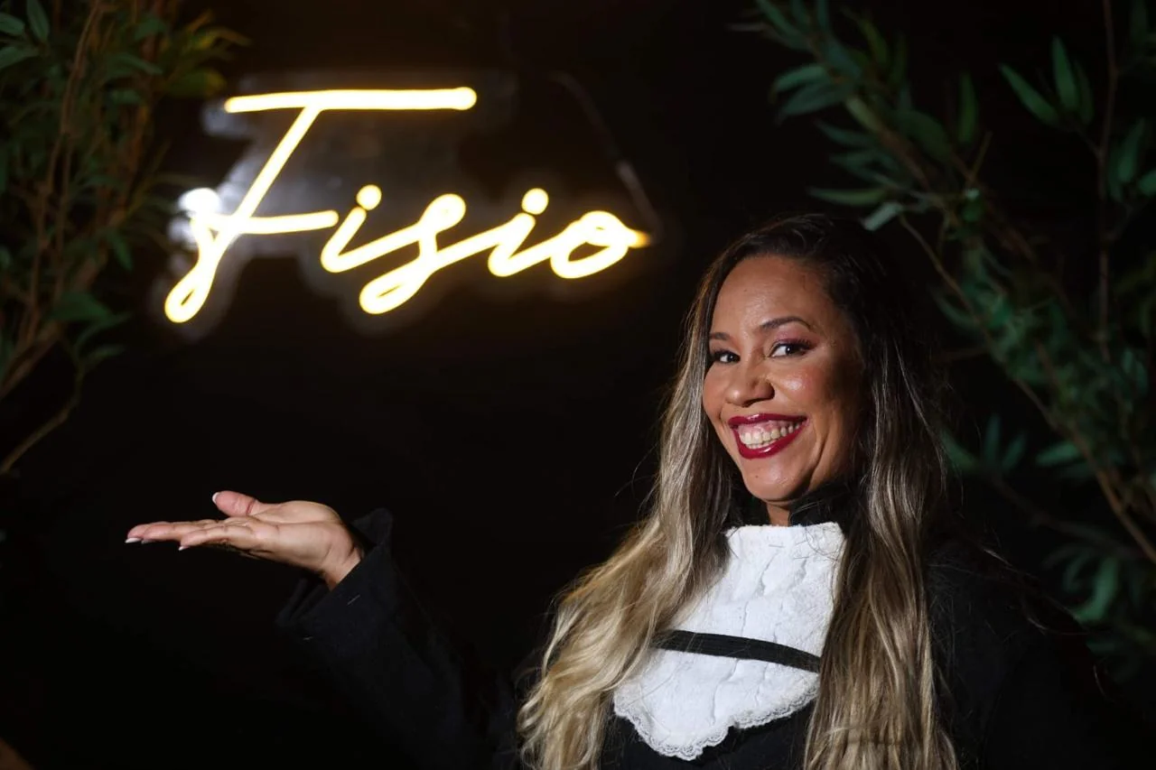 Dra. Aline Gonzaga ao lado de uma iluminação decorativa com a palavra Fisio