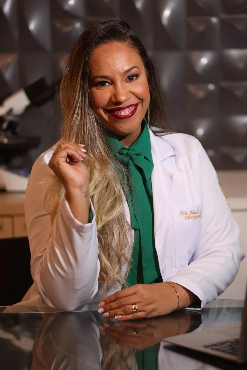 Dra. Aline Gonzaga sorrindo, com jaleco branco, em ambiente profissional